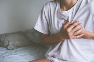 Picture of a woman holding her chest in pain while sitting on a bed.