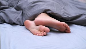 Picture of two feet on a bed, under a comforter.
