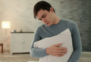 Picture of a young man holding a pillow and sleepwalking.
